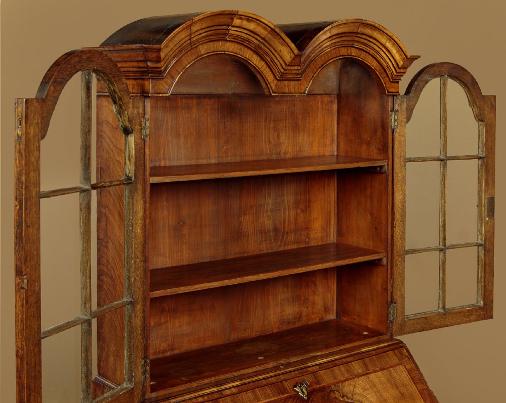 A Queen Anne style walnut bureau bookcase featuring a double-domed top, glazed upper doors, a slant-front writing slope, lower drawers with a carved shell motif, and slender cabriole legs. View VII