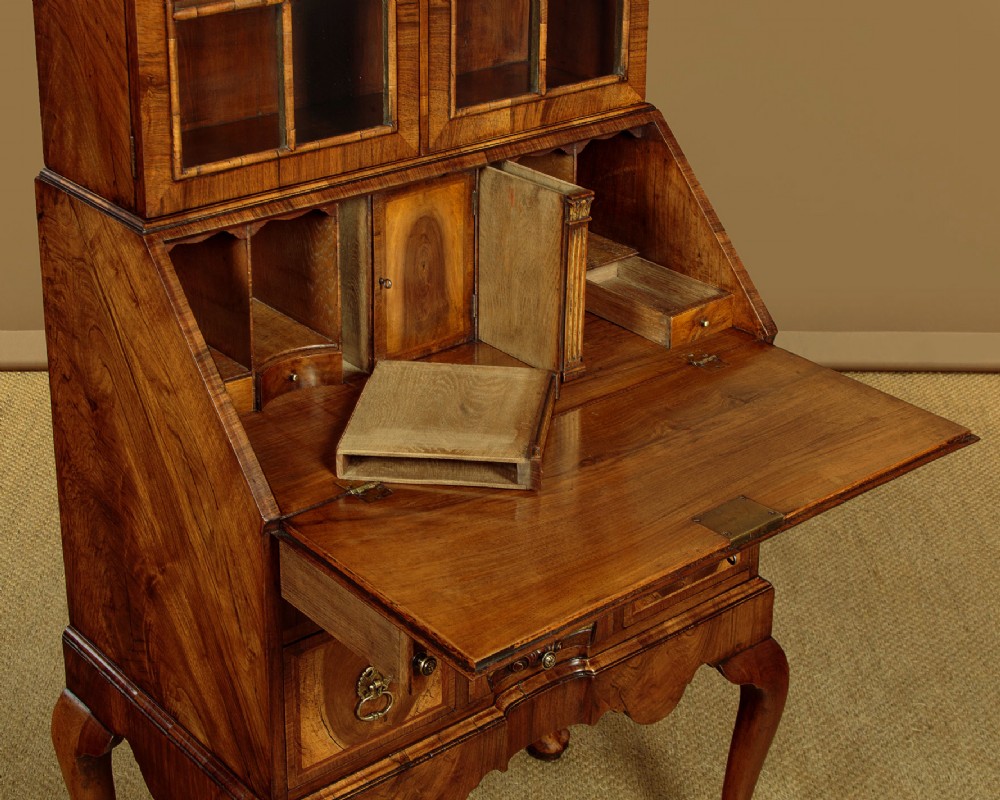 A Queen Anne style walnut bureau bookcase featuring a double-domed top, glazed upper doors, a slant-front writing slope, lower drawers with a carved shell motif, and slender cabriole legs. View X