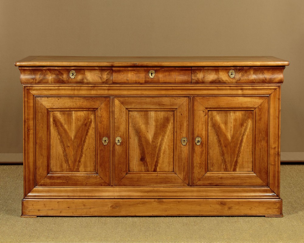A 19th-century French cherrywood enfilade featuring three drawers over three panelled doors with geometric wood grain and brass escutcheons.
