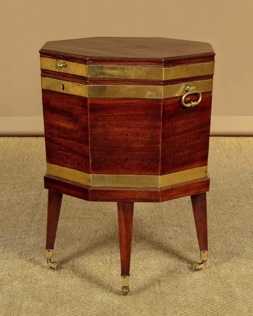 An octagonal Georgian mahogany cellarette bound in brass bands on tapered legs with castors. View II