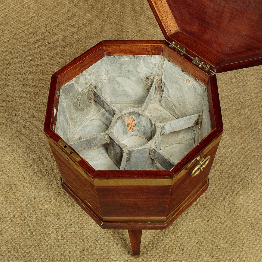 An octagonal Georgian mahogany cellarette bound in brass bands on tapered legs with castors. View IV