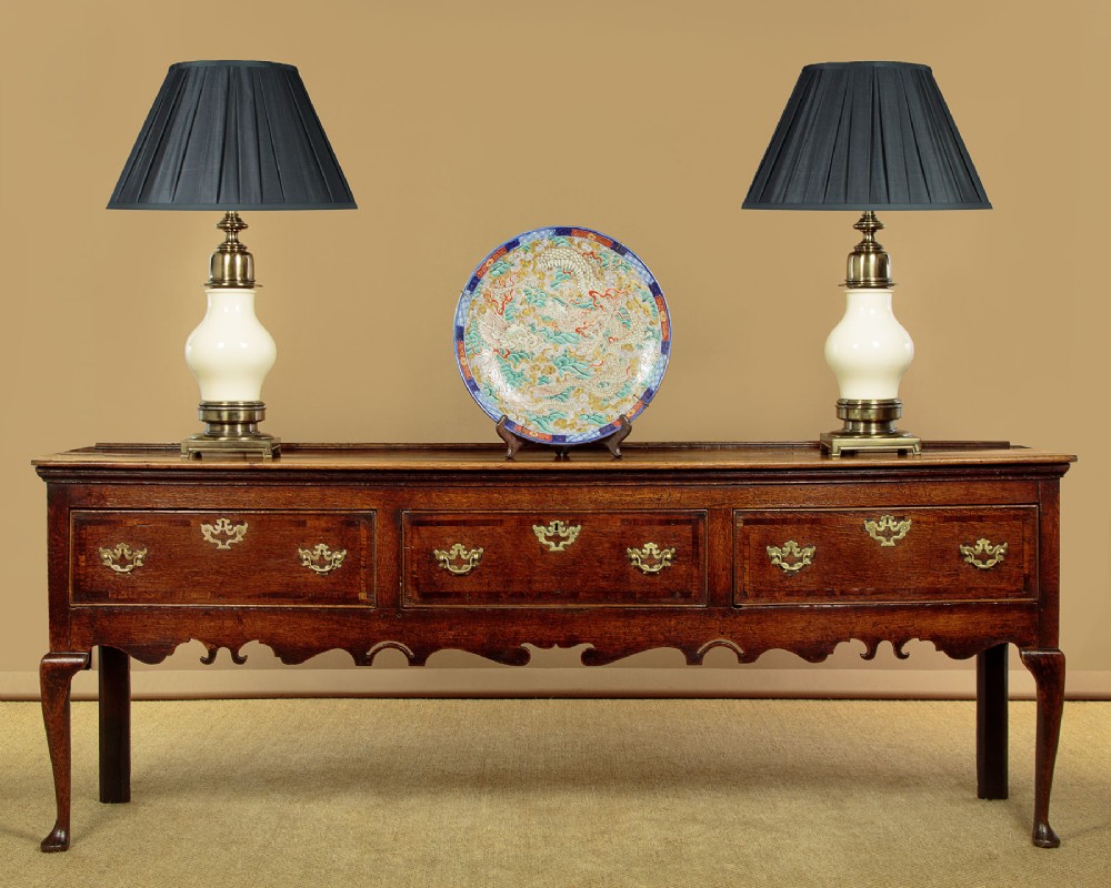 An eighteenth-century dark oak dresser base featuring three drawers with brass handles, a scalloped apron, and front cabriole legs. View II