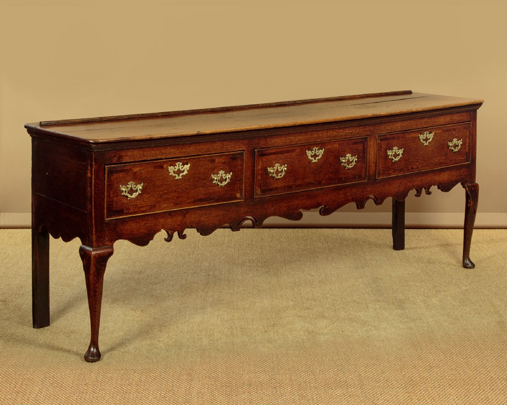 An eighteenth-century dark oak dresser base featuring three drawers with brass handles, a scalloped apron, and front cabriole legs. View III