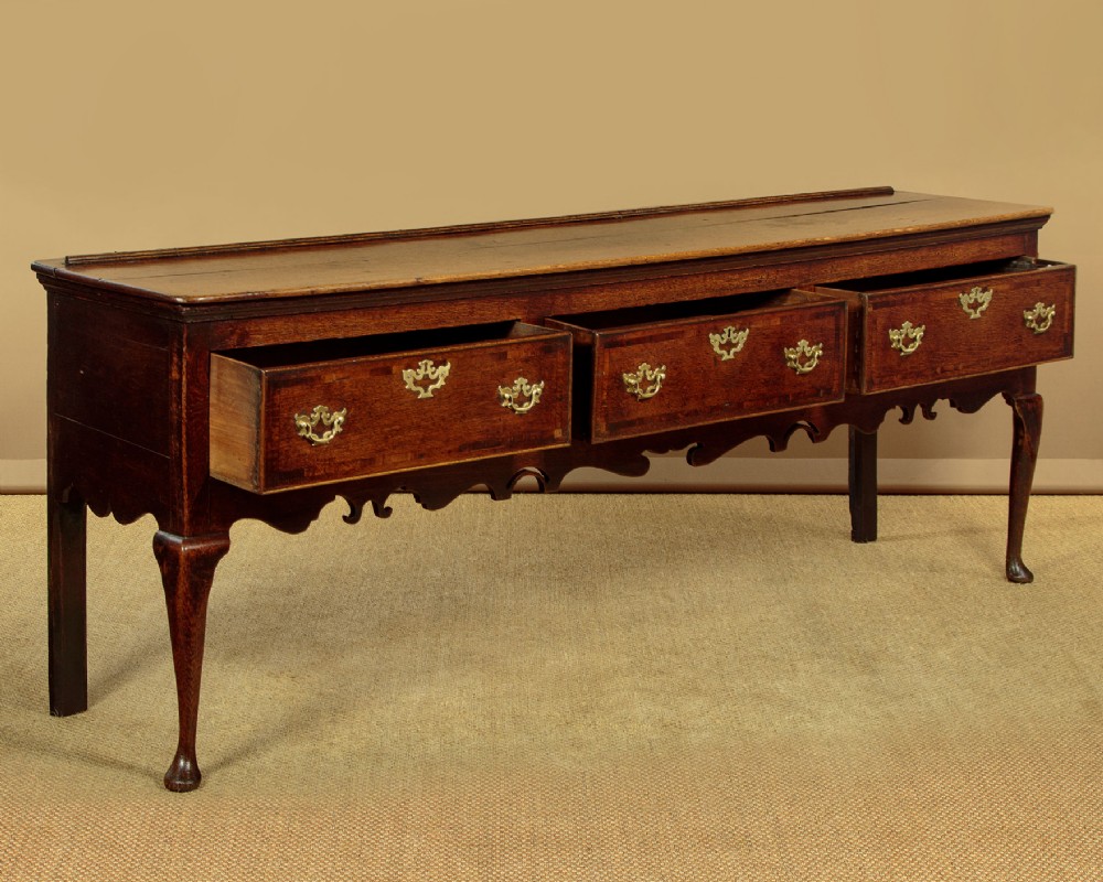 An eighteenth-century dark oak dresser base featuring three drawers with brass handles, a scalloped apron, and front cabriole legs. View IV