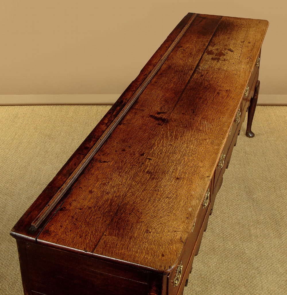 An eighteenth-century dark oak dresser base featuring three drawers with brass handles, a scalloped apron, and front cabriole legs. View V