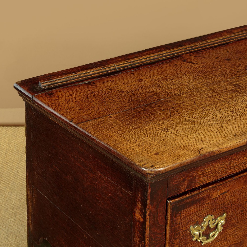 An eighteenth-century dark oak dresser base featuring three drawers with brass handles, a scalloped apron, and front cabriole legs. View VI
