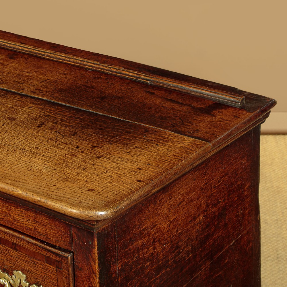 An eighteenth-century dark oak dresser base featuring three drawers with brass handles, a scalloped apron, and front cabriole legs. View VII