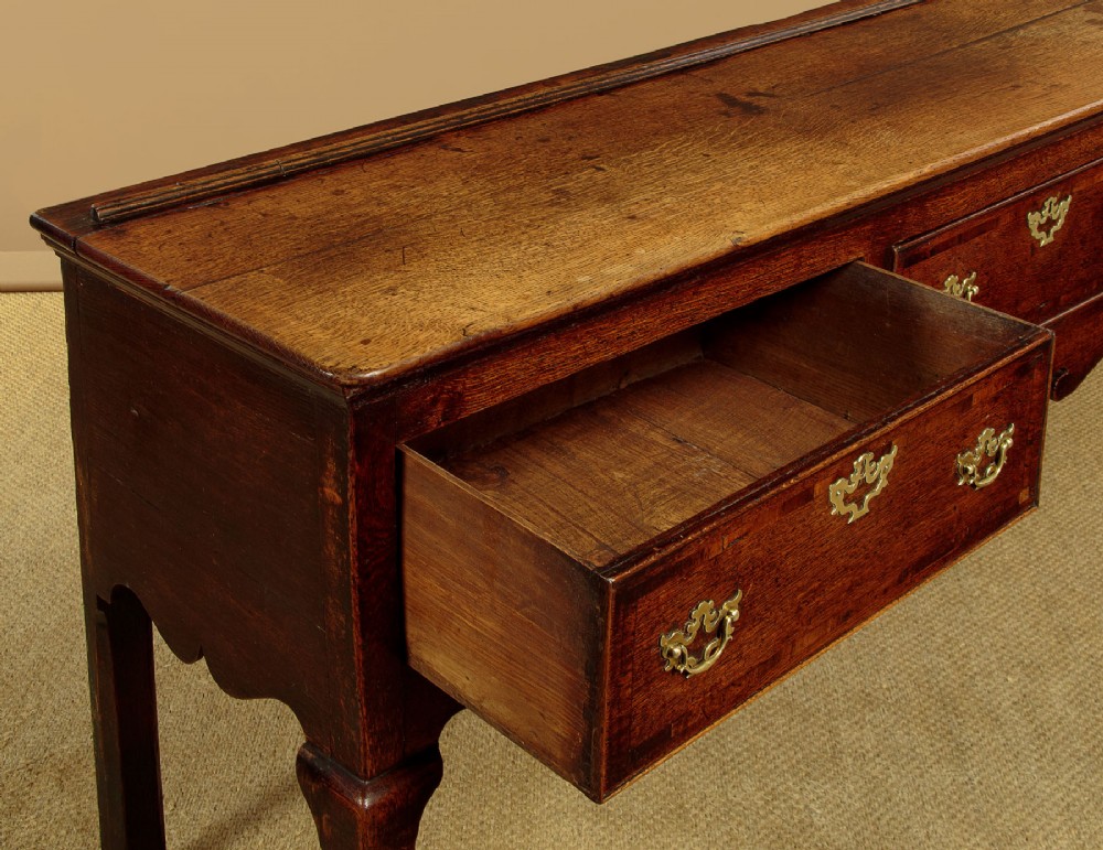 An eighteenth-century dark oak dresser base featuring three drawers with brass handles, a scalloped apron, and front cabriole legs. View VIII
