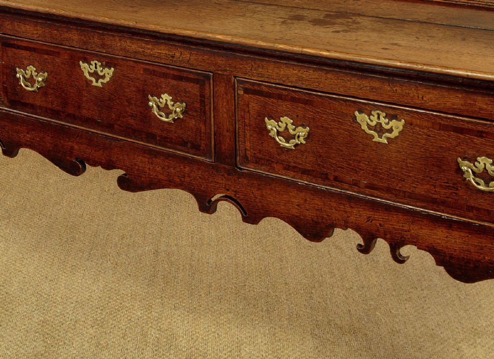 An eighteenth-century dark oak dresser base featuring three drawers with brass handles, a scalloped apron, and front cabriole legs. View IX