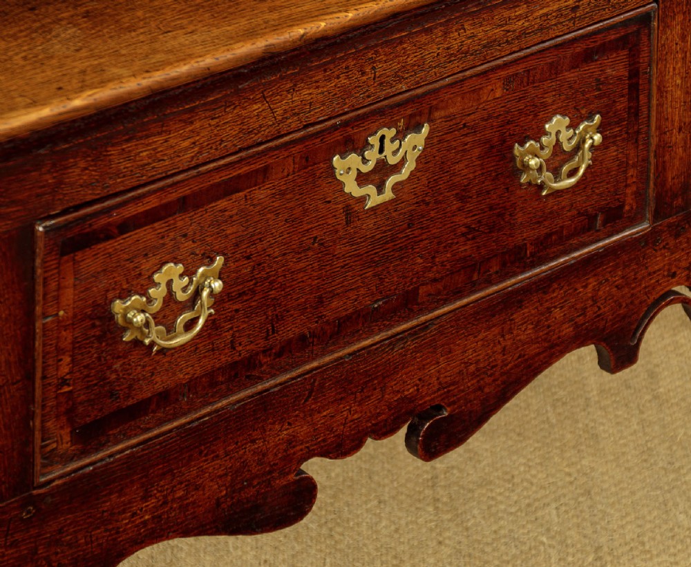 An eighteenth-century dark oak dresser base featuring three drawers with brass handles, a scalloped apron, and front cabriole legs. View X