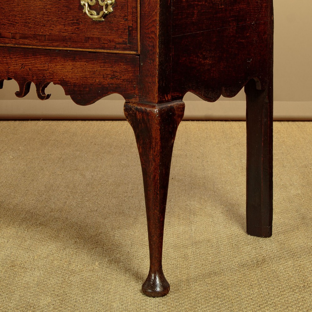 An eighteenth-century dark oak dresser base featuring three drawers with brass handles, a scalloped apron, and front cabriole legs. View XI