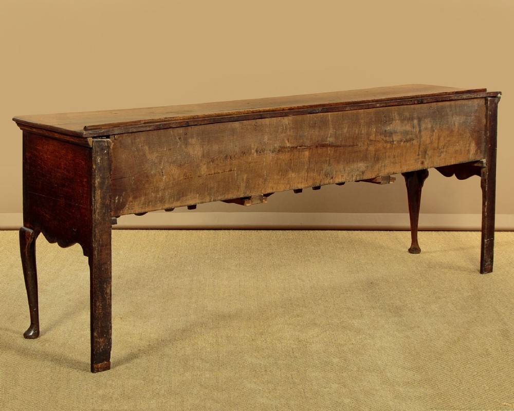 An eighteenth-century dark oak dresser base featuring three drawers with brass handles, a scalloped apron, and front cabriole legs. View XII