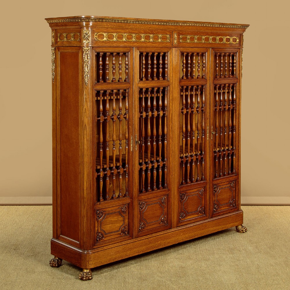 A large four-door oak bookcase featuring decorative turned spindles on the upper door sections, gilded brass frieze mounts, and carved lower timber panels. View II