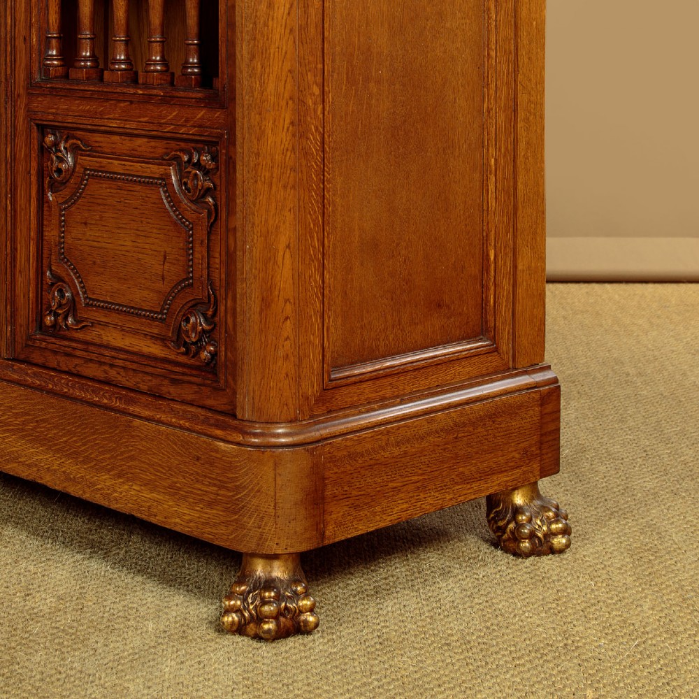 A large four-door oak bookcase featuring decorative turned spindles on the upper door sections, gilded brass frieze mounts, and carved lower timber panels. View XII
