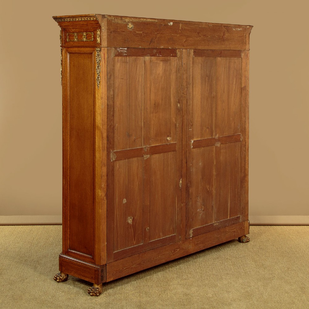 A large four-door oak bookcase featuring decorative turned spindles on the upper door sections, gilded brass frieze mounts, and carved lower timber panels. View XIII