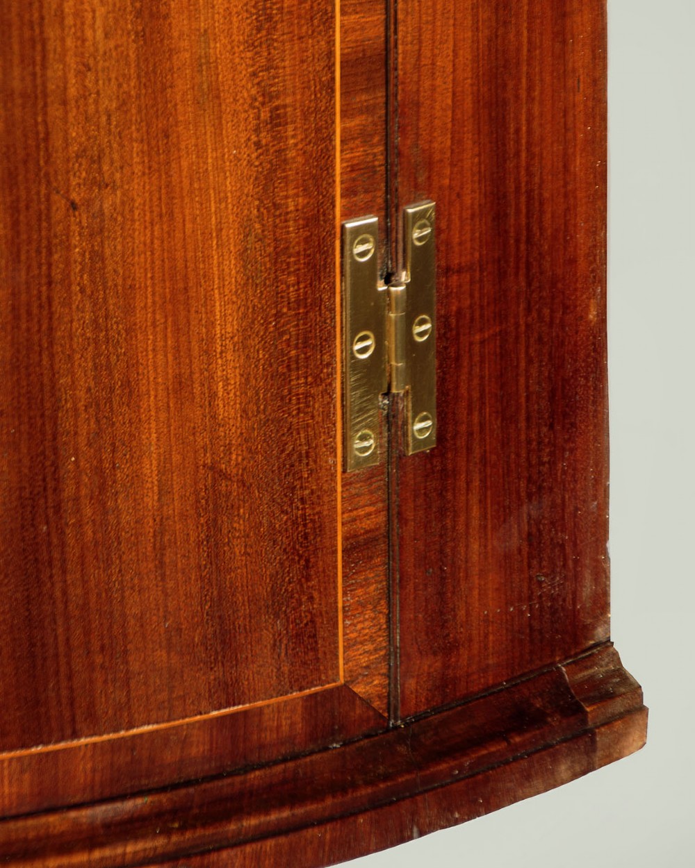 A George III bow-front mahogany corner cupboard featuring twin doors with inlaid fan motifs, crossbanded borders, and brass H-hinges. View VI