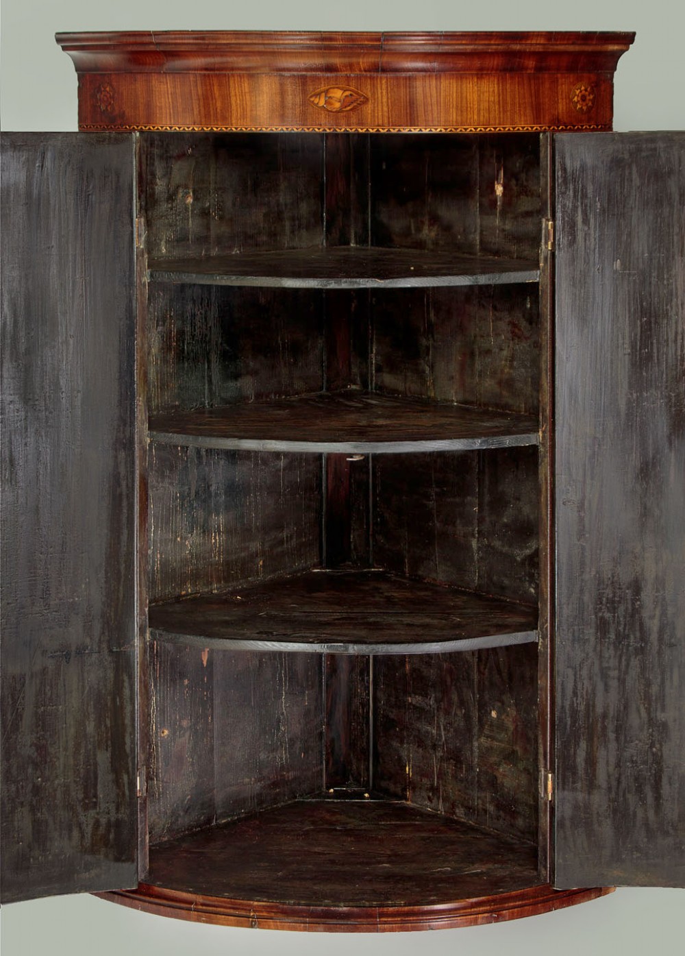 A George III bow-front mahogany corner cupboard featuring twin doors with inlaid fan motifs, crossbanded borders, and brass H-hinges. View VII