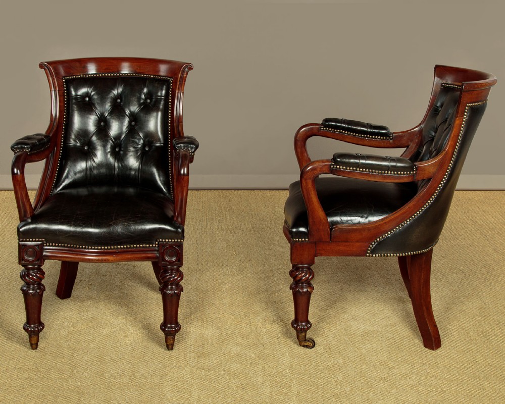 A pair of William IV mahogany library chairs featuring deep-buttoned dark leather upholstery, padded armrests, brass stud trim, turned carved front legs, and castors. View II
