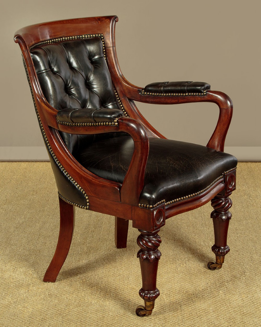 A pair of William IV mahogany library chairs featuring deep-buttoned dark leather upholstery, padded armrests, brass stud trim, turned carved front legs, and castors. View III