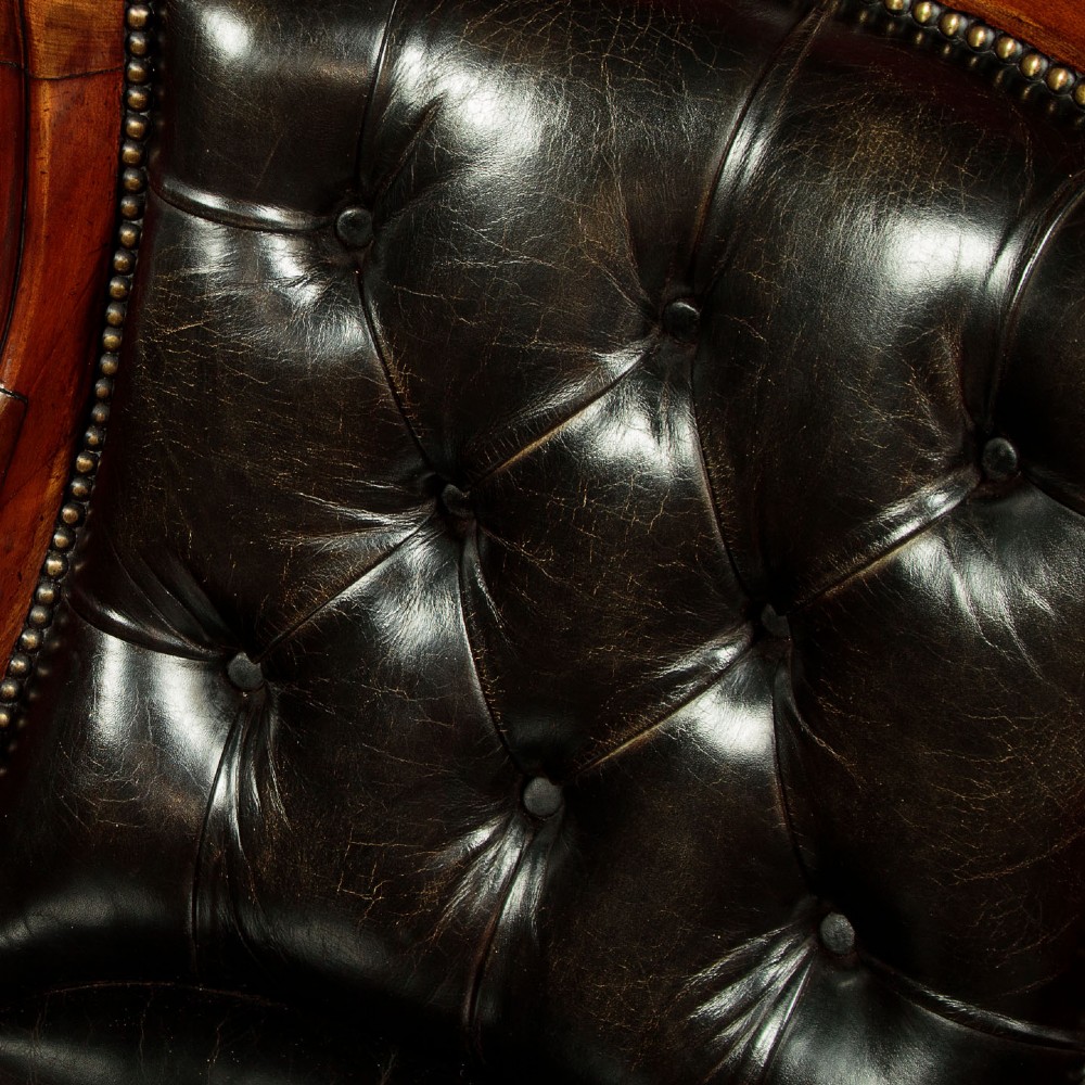 A pair of William IV mahogany library chairs featuring deep-buttoned dark leather upholstery, padded armrests, brass stud trim, turned carved front legs, and castors. View VII