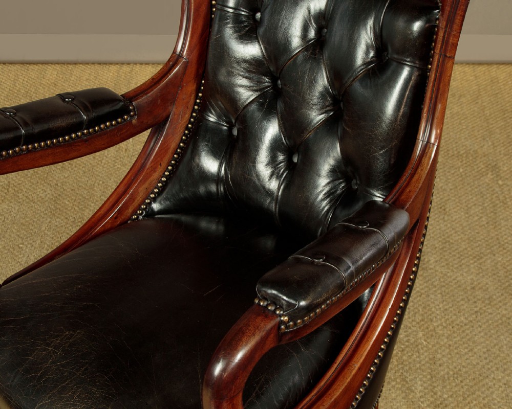 A pair of William IV mahogany library chairs featuring deep-buttoned dark leather upholstery, padded armrests, brass stud trim, turned carved front legs, and castors. View VIII