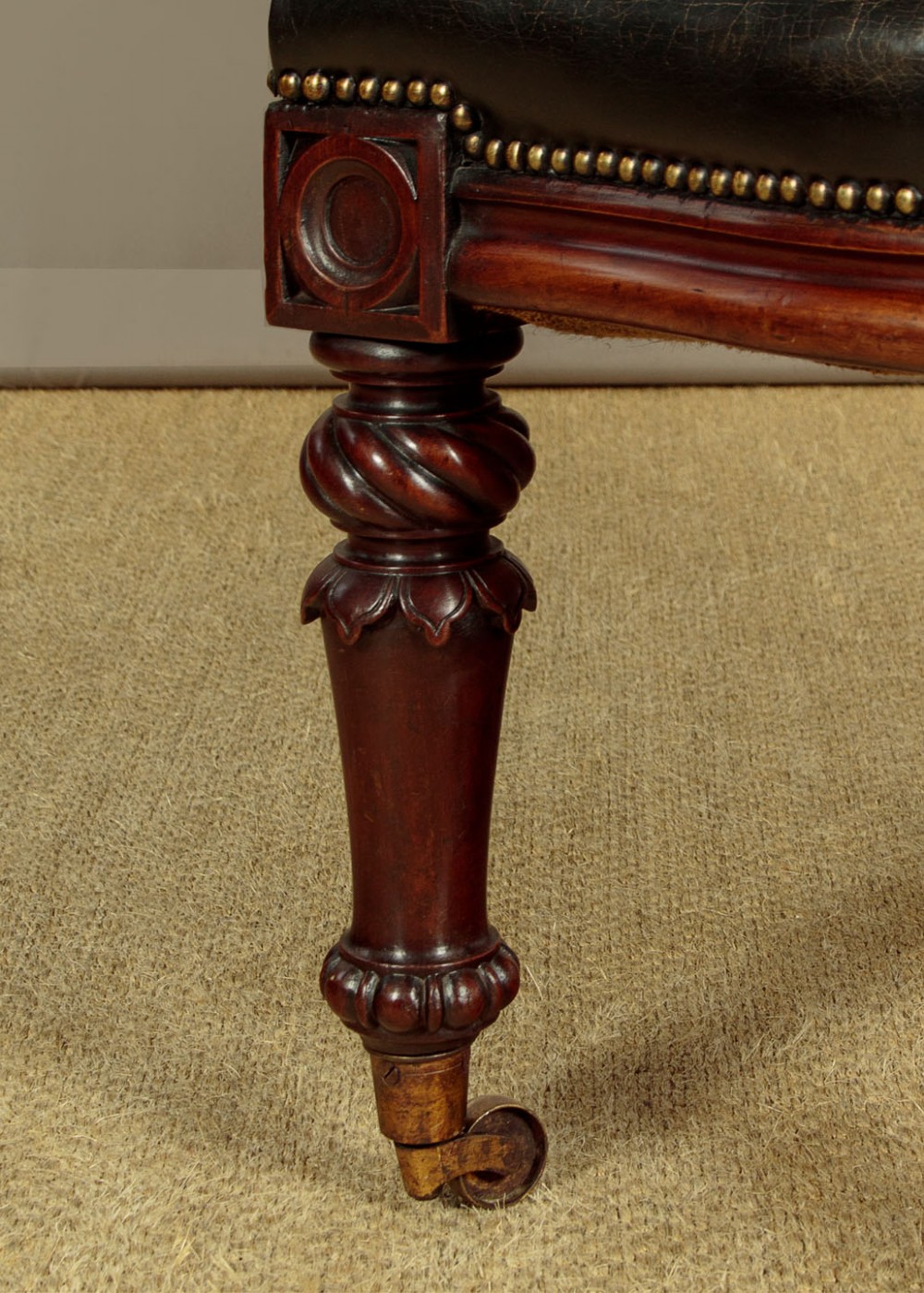 A pair of William IV mahogany library chairs featuring deep-buttoned dark leather upholstery, padded armrests, brass stud trim, turned carved front legs, and castors. View XI