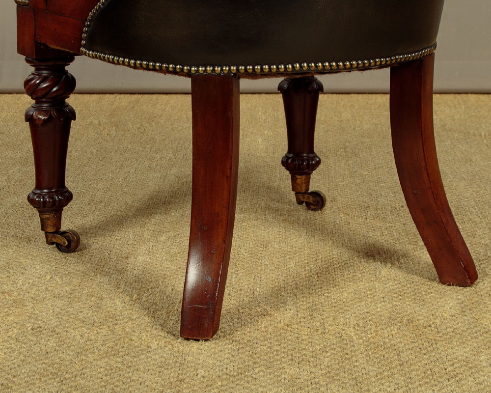 A pair of William IV mahogany library chairs featuring deep-buttoned dark leather upholstery, padded armrests, brass stud trim, turned carved front legs, and castors. View XIII
