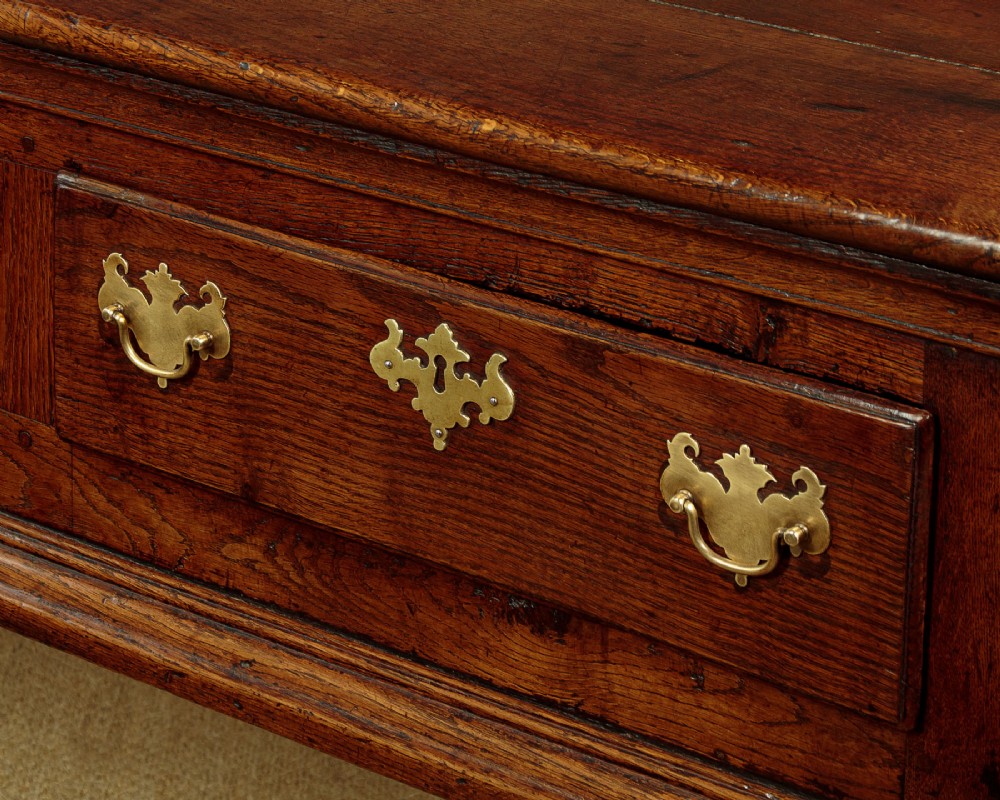 An 18th-century dark oak dresser base featuring three inline drawers with decorative brass drop handles and turned front legs. View VIII