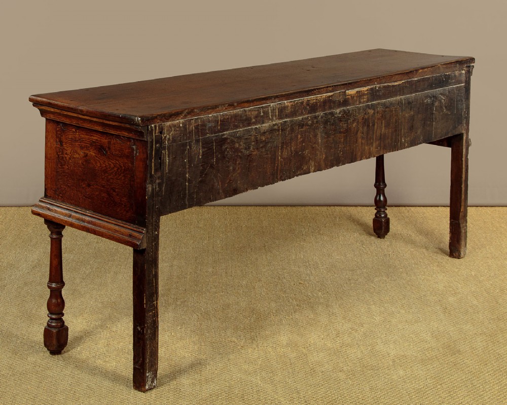 An 18th-century dark oak dresser base featuring three inline drawers with decorative brass drop handles and turned front legs. View XI