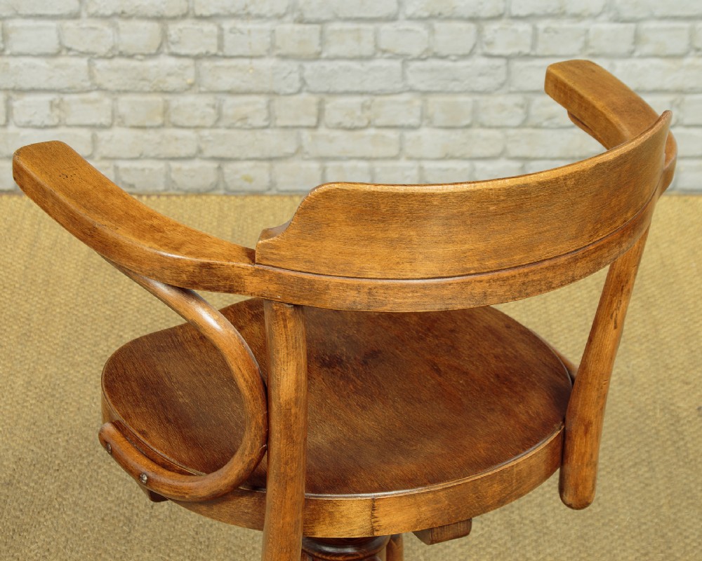A pair of antique warm brown bentwood swivel desk chairs with curved armrests and quadruped pedestal bases. View V