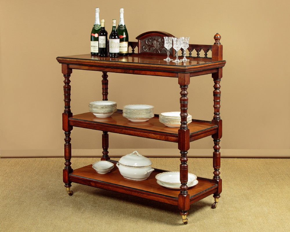 An Aesthetic Movement three-tier walnut buffet featuring turned corner columns, a carved floral back gallery, and brass castors. View II