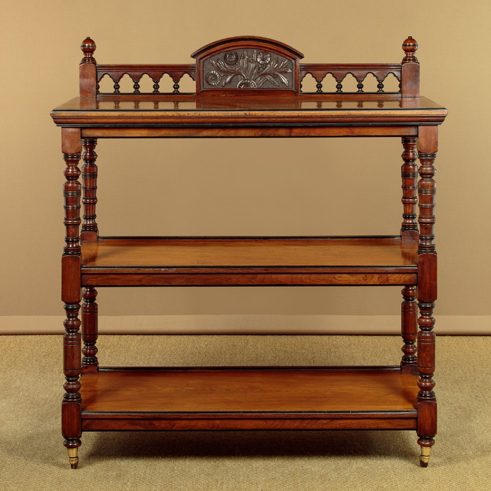 An Aesthetic Movement three-tier walnut buffet featuring turned corner columns, a carved floral back gallery, and brass castors. View III