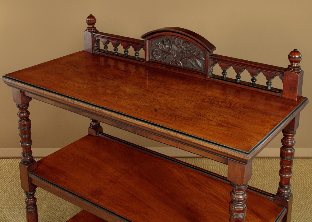An Aesthetic Movement three-tier walnut buffet featuring turned corner columns, a carved floral back gallery, and brass castors. View IV