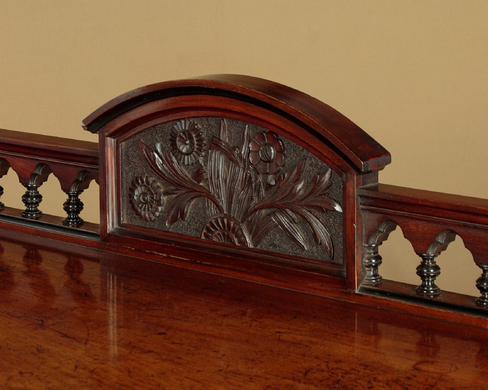 An Aesthetic Movement three-tier walnut buffet featuring turned corner columns, a carved floral back gallery, and brass castors. View V