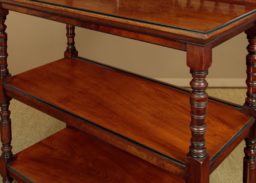 An Aesthetic Movement three-tier walnut buffet featuring turned corner columns, a carved floral back gallery, and brass castors. View VII