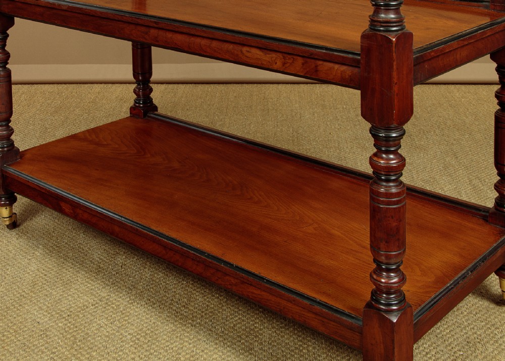 An Aesthetic Movement three-tier walnut buffet featuring turned corner columns, a carved floral back gallery, and brass castors. View IX