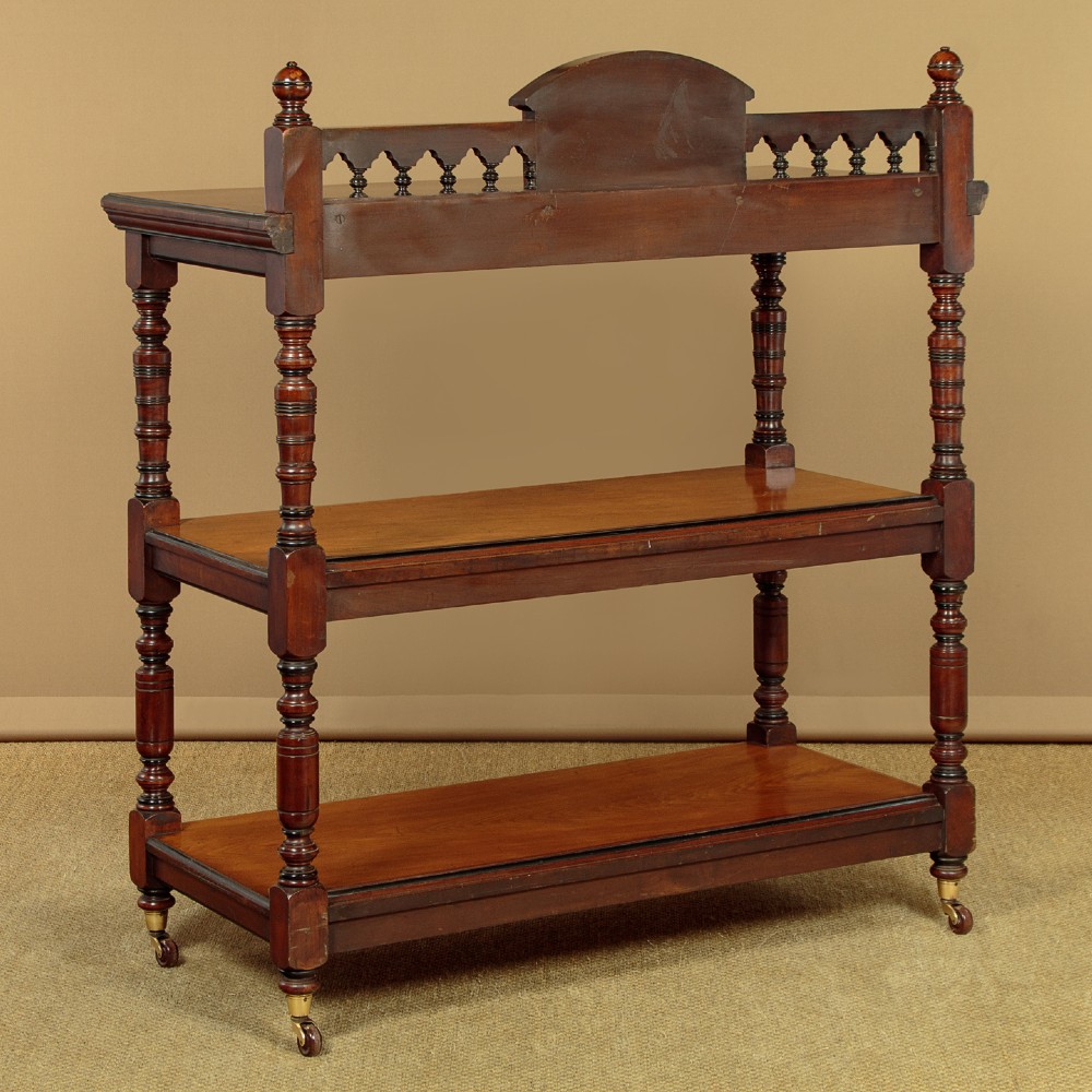 An Aesthetic Movement three-tier walnut buffet featuring turned corner columns, a carved floral back gallery, and brass castors. View XII