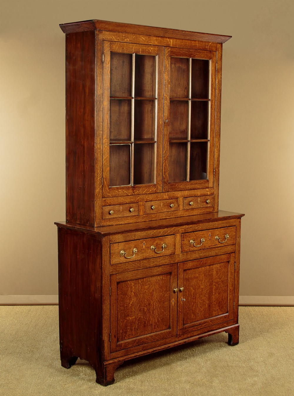 A Georgian Welsh oak cwpwrdd gwydr featuring a glazed upper section with two six-pane glass doors above three small drawers, resting on a base cabinet with two drawers over a panelled double cupboard.