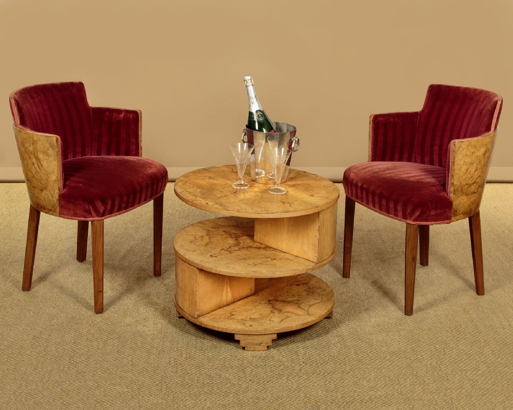 A circular three-tiered Art Deco coffee table constructed from warm golden burr timber veneer with offset geometric supports. View II