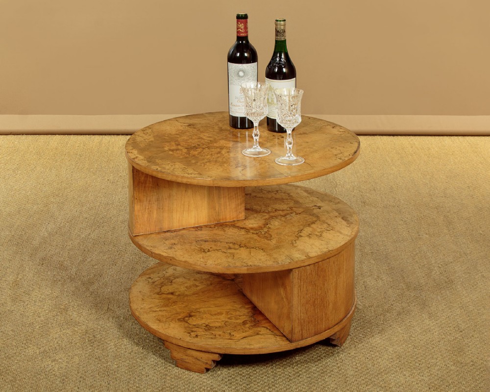 A circular three-tiered Art Deco coffee table constructed from warm golden burr timber veneer with offset geometric supports. View III