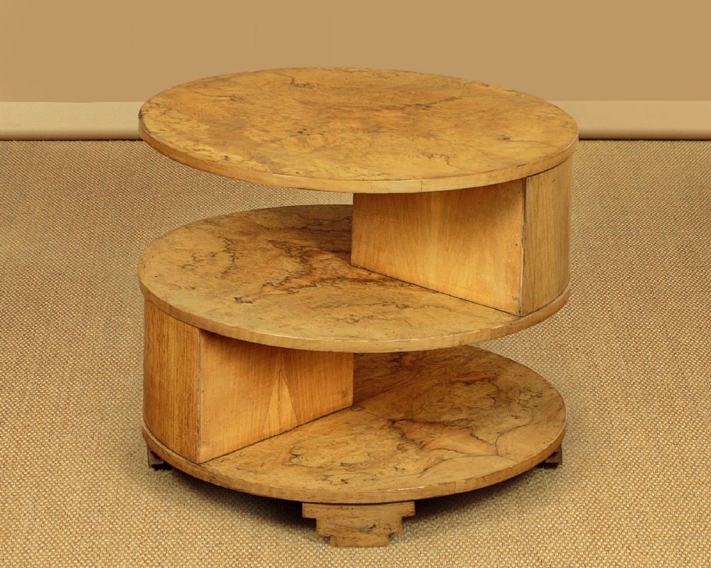 A circular three-tiered Art Deco coffee table constructed from warm golden burr timber veneer with offset geometric supports. View IV