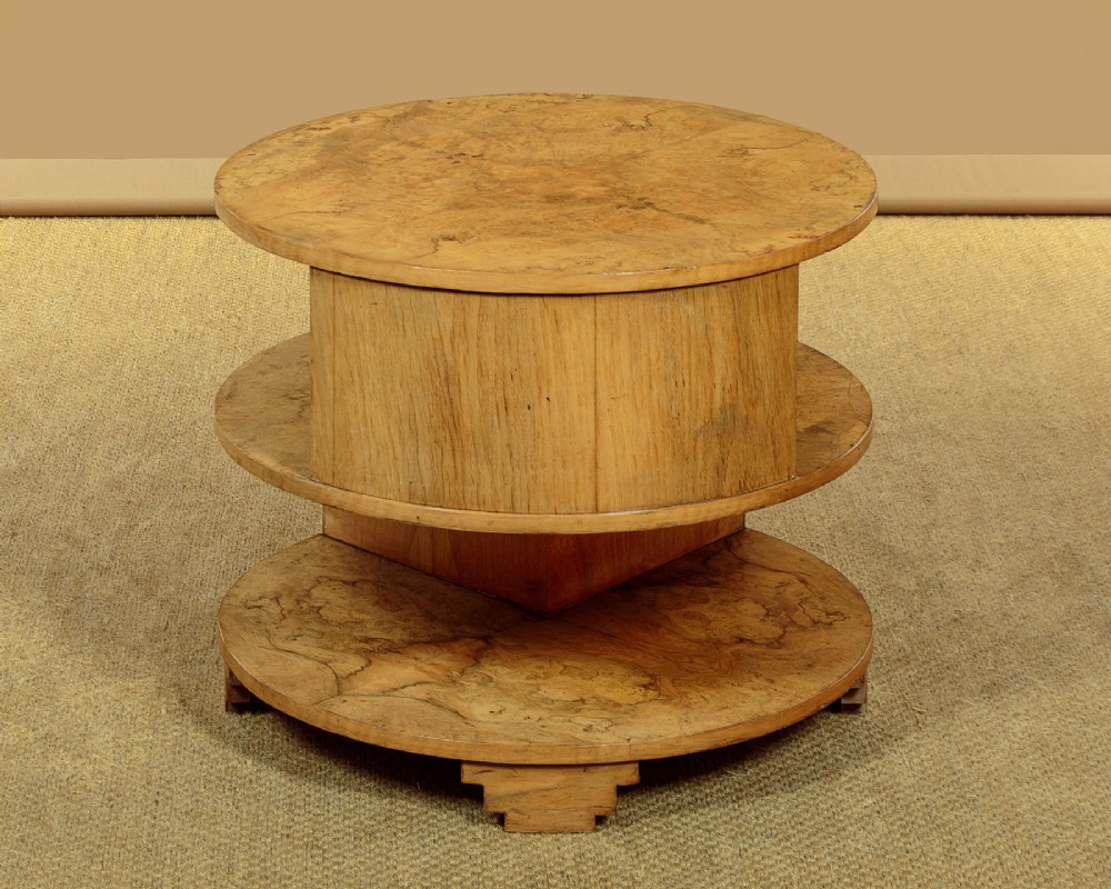 A circular three-tiered Art Deco coffee table constructed from warm golden burr timber veneer with offset geometric supports. View V