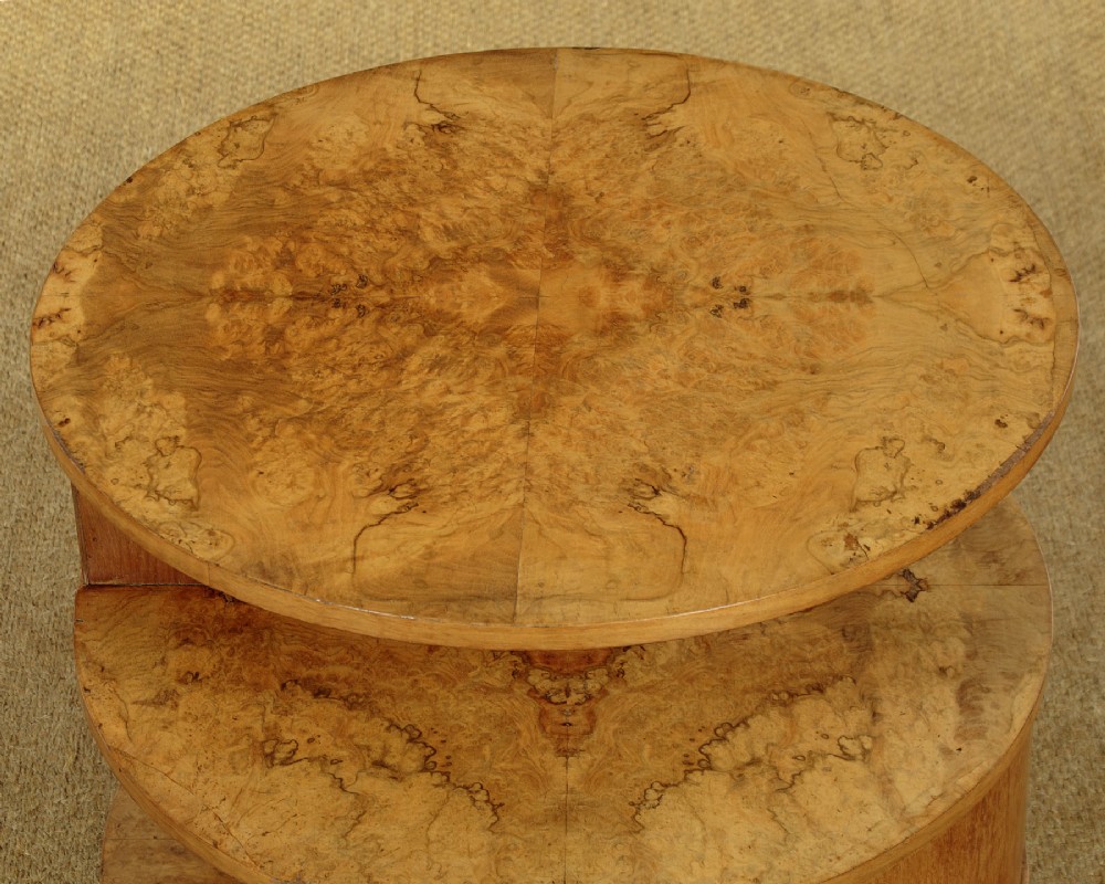A circular three-tiered Art Deco coffee table constructed from warm golden burr timber veneer with offset geometric supports. View VI