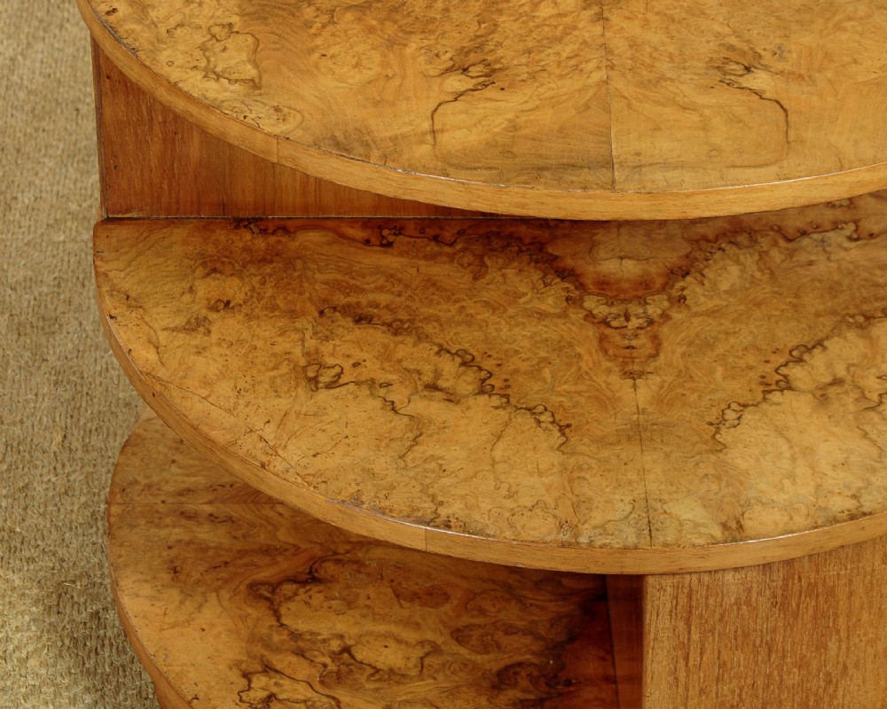 A circular three-tiered Art Deco coffee table constructed from warm golden burr timber veneer with offset geometric supports. View VII