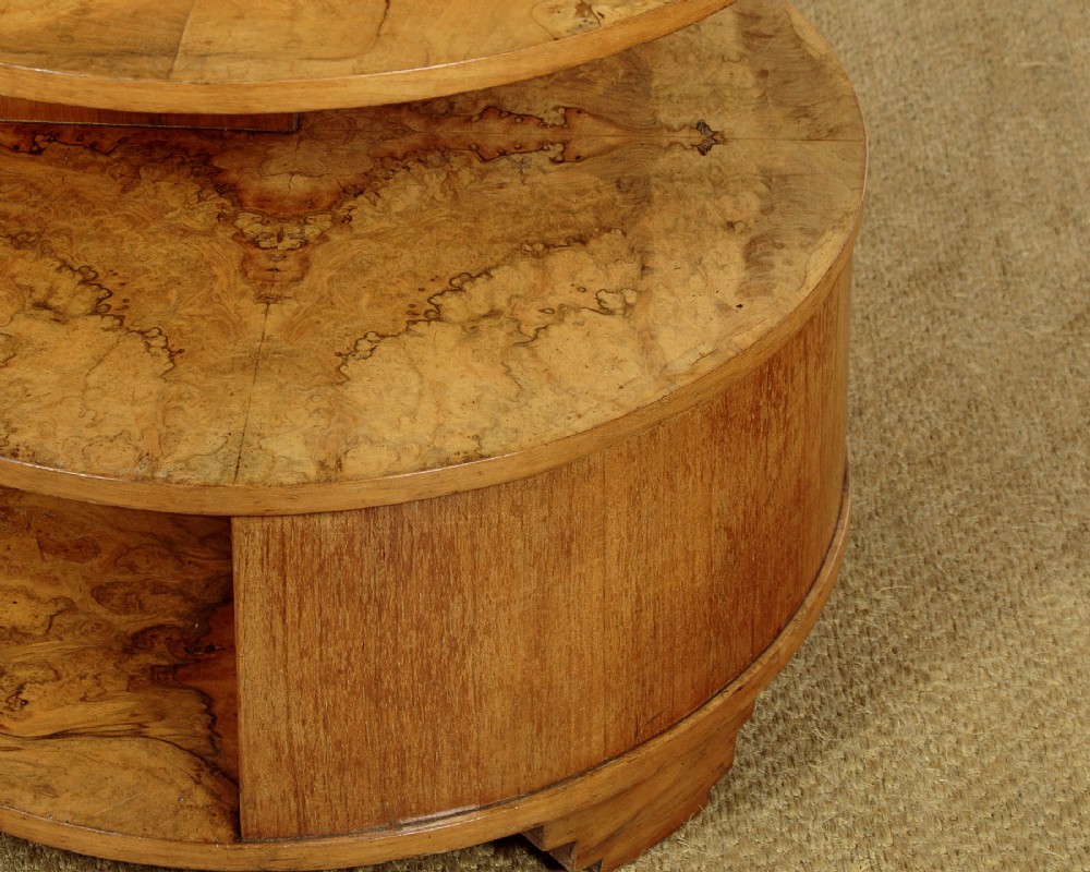 A circular three-tiered Art Deco coffee table constructed from warm golden burr timber veneer with offset geometric supports. View VIII