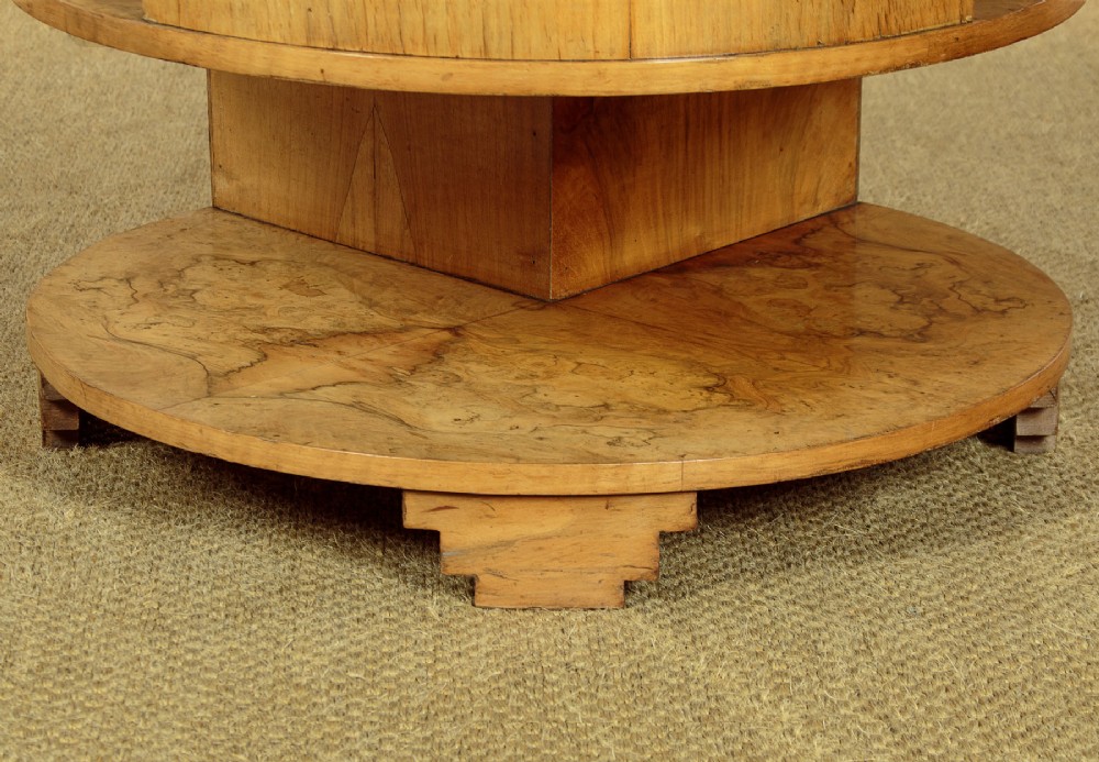 A circular three-tiered Art Deco coffee table constructed from warm golden burr timber veneer with offset geometric supports. View X