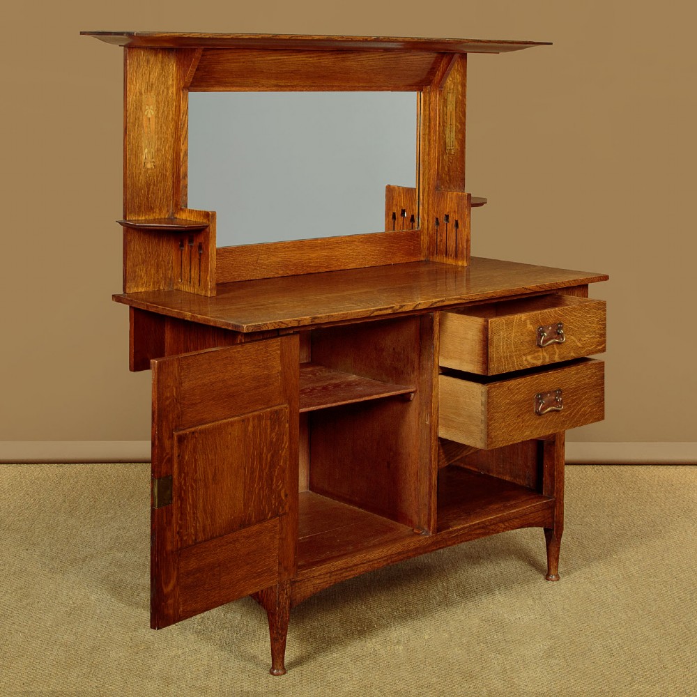 An Arts and Crafts quarter-sawn oak dresser featuring a mirrored top structure with small display shelves, inlaid floral details, hammered copper strap hinges, two drawers, and a lower cupboard. View IV