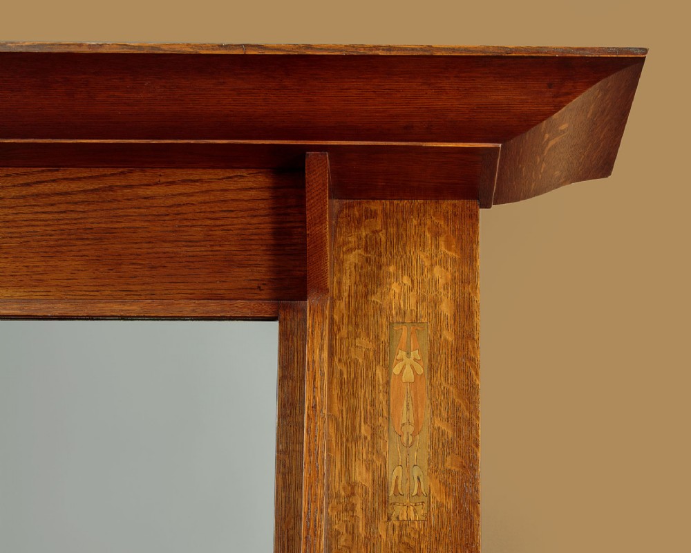 An Arts and Crafts quarter-sawn oak dresser featuring a mirrored top structure with small display shelves, inlaid floral details, hammered copper strap hinges, two drawers, and a lower cupboard. View VI