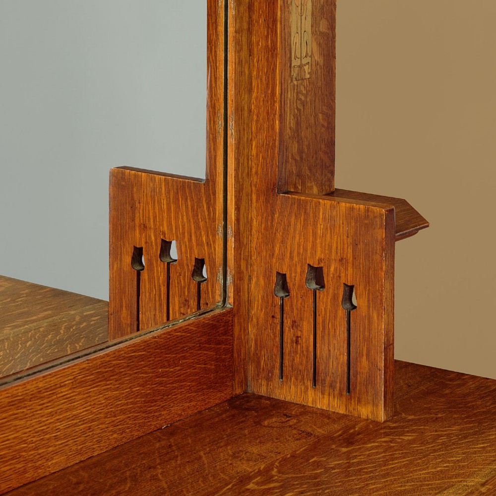 An Arts and Crafts quarter-sawn oak dresser featuring a mirrored top structure with small display shelves, inlaid floral details, hammered copper strap hinges, two drawers, and a lower cupboard. View VIII