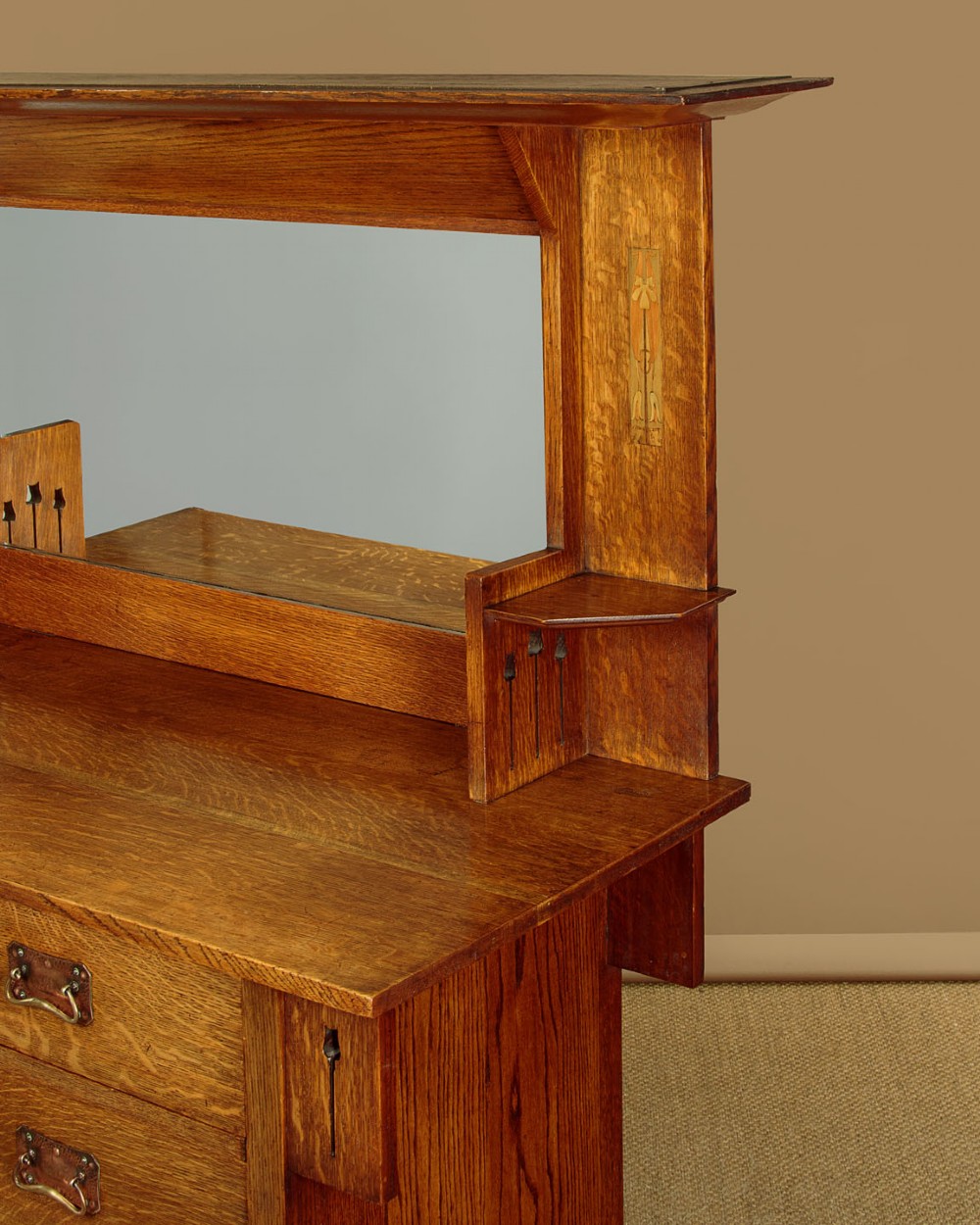An Arts and Crafts quarter-sawn oak dresser featuring a mirrored top structure with small display shelves, inlaid floral details, hammered copper strap hinges, two drawers, and a lower cupboard. View XIV